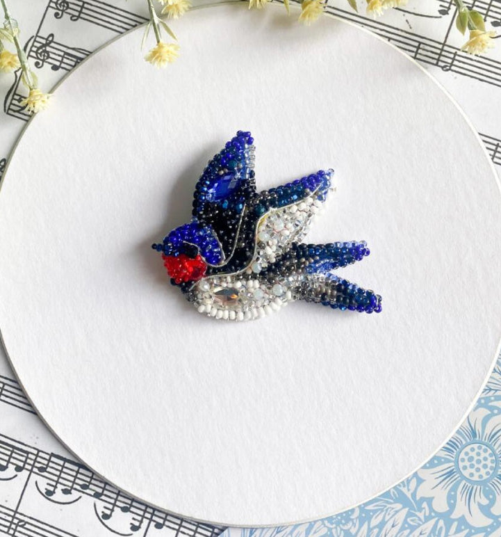 Decorative brooch with blue, red, and silver colors on a white plate with musical notes and flowers.