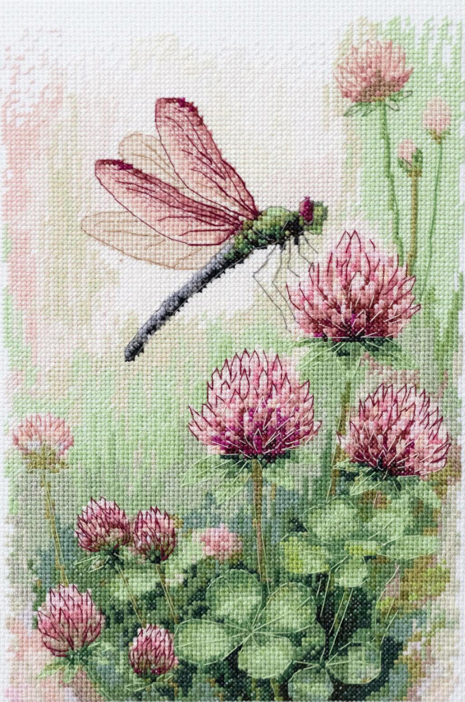 Cross-stitched design of a dragonfly and pink flowers on a white background