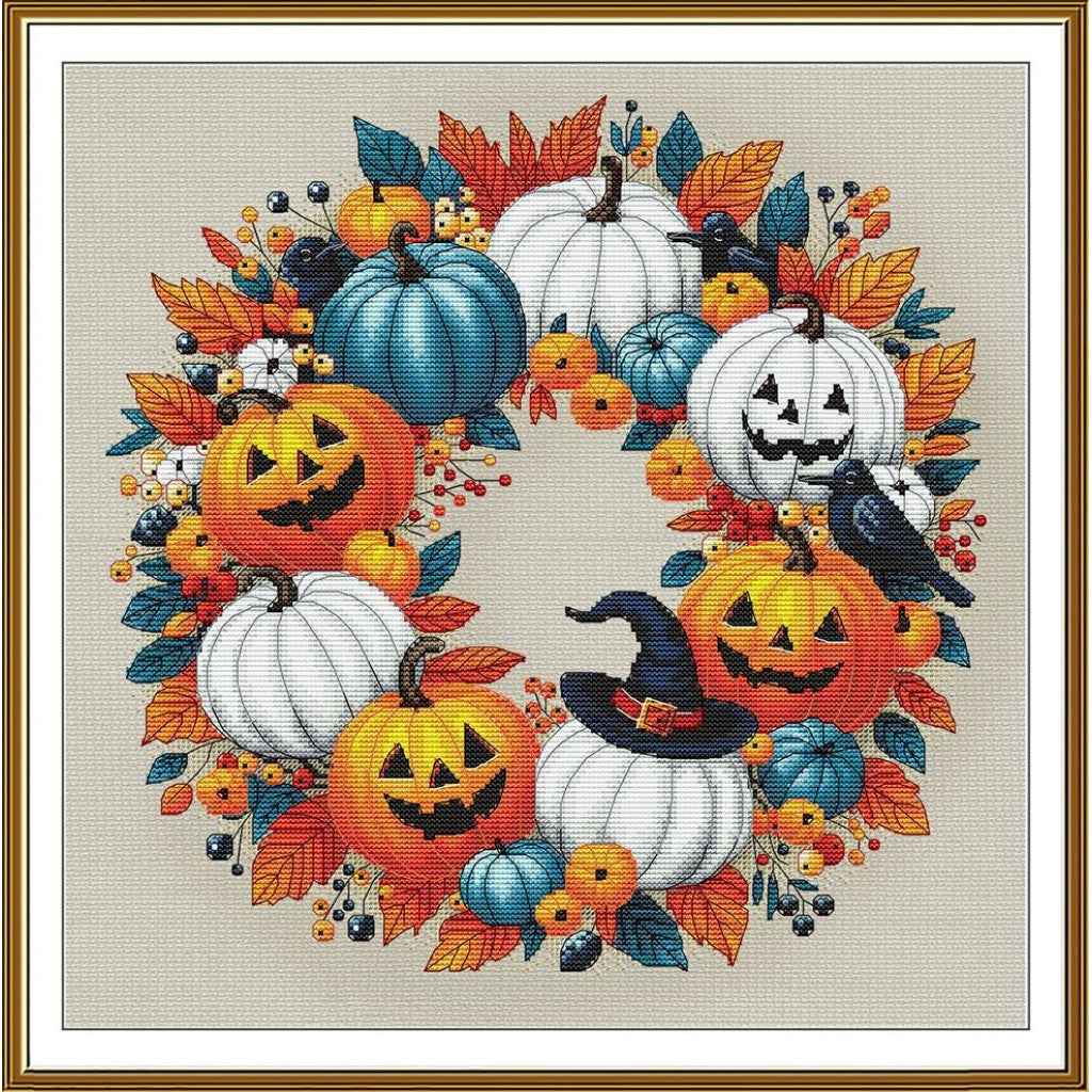 A framed cross-stitch or needlework design featuring a circular autumn wreath with orange jack-o'-lanterns, white pumpkins, blue gourds, orange and teal leaves, small white flowers, berries, and a black witch's hat, surrounded by a gold-toned frame and white mat.