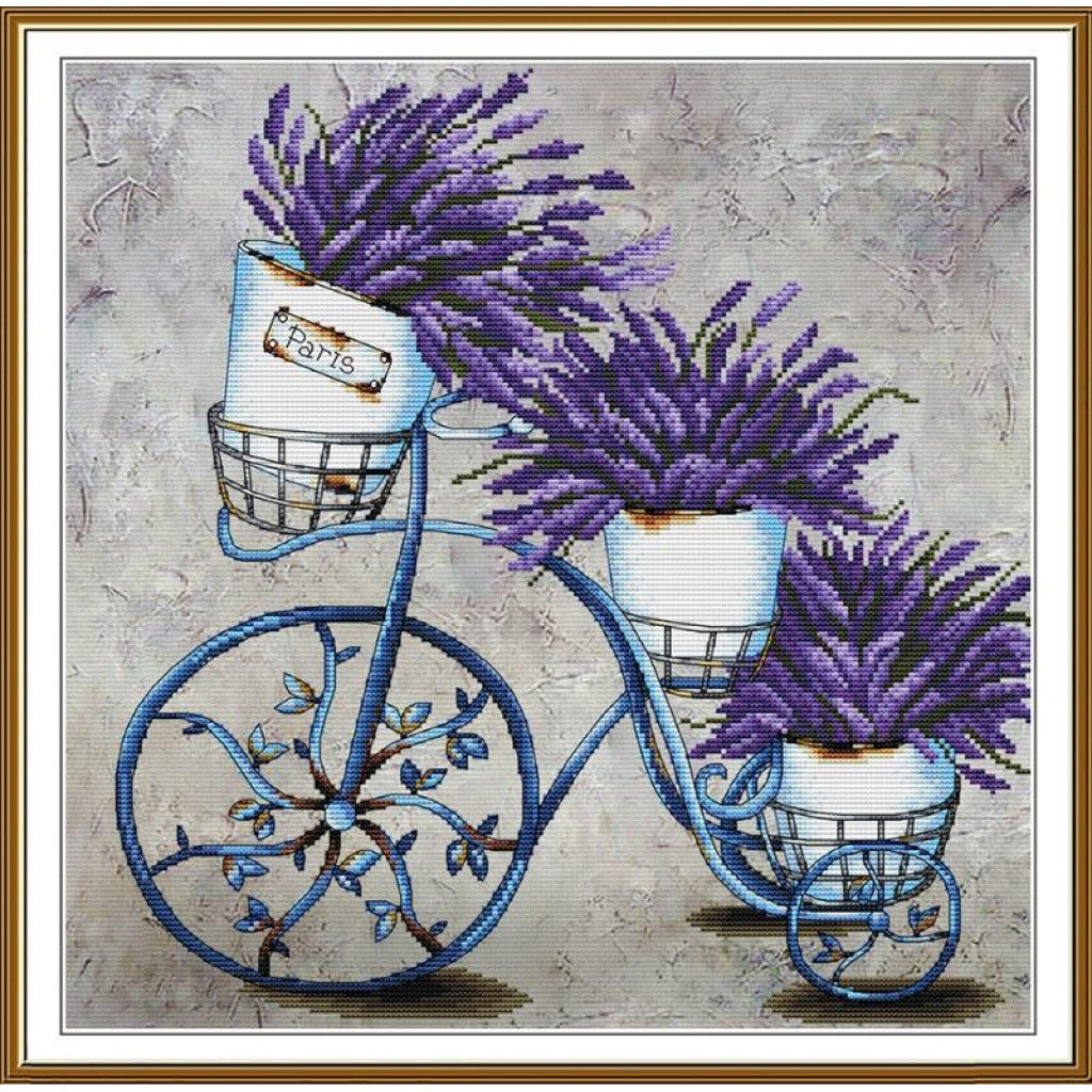 A framed decorative artwork showing a blue bicycle with three white baskets filled with purple lavender flowers, set against a textured light gray background.