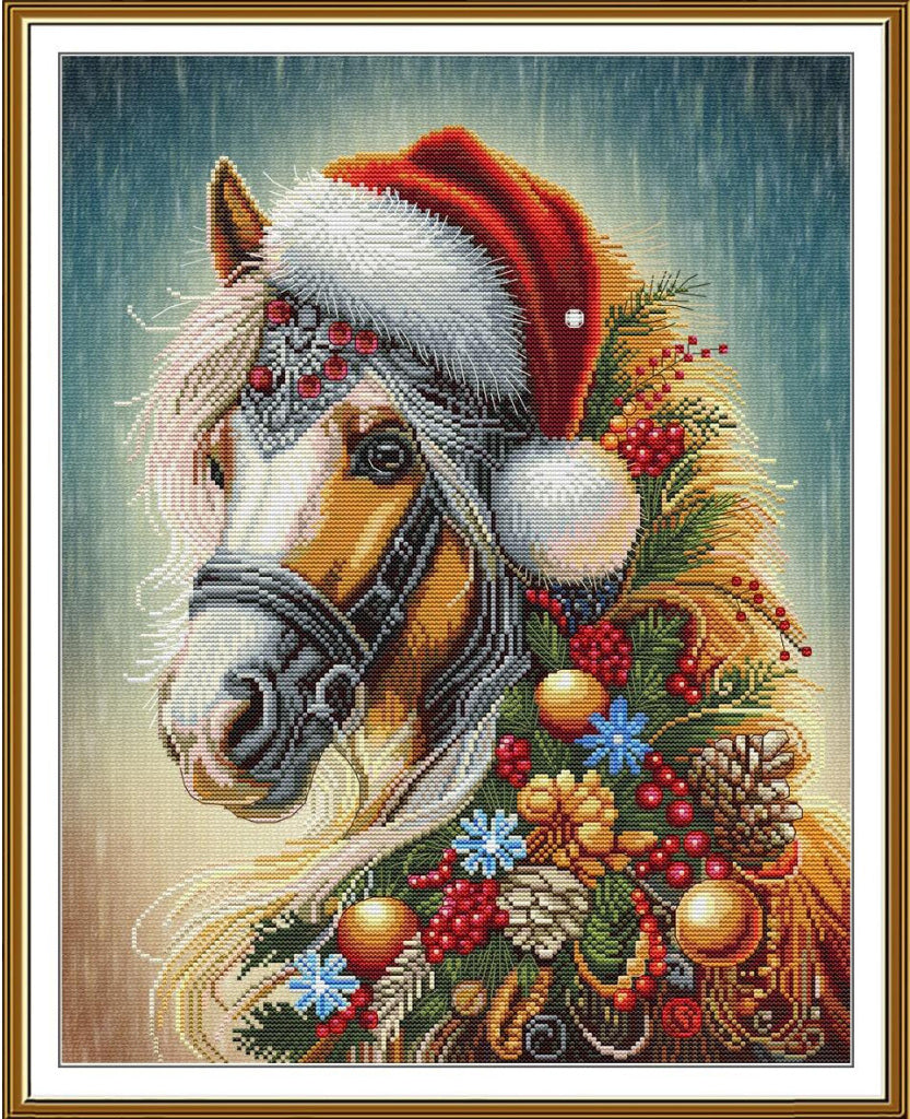 A framed needlepoint or cross-stitch style artwork showing a horse in profile wearing a red Santa hat, surrounded by holiday greenery, pinecones, ornaments, and berries on a blue-gray background.
