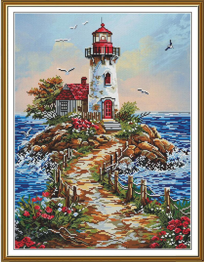 A framed needlepoint or cross-stitch style lighthouse scene with a white tower, red roof and door, rocky island, blue water, sky, birds, and flowers. The artwork is shown within a white mat and gold-toned frame.