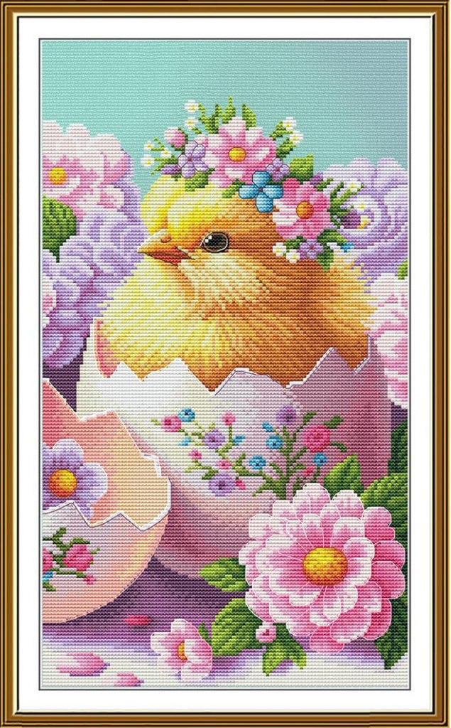 A framed cross-stitch or needlework design featuring a yellow chick hatching from a pink egg, surrounded by pink flowers and green leaves, with a light blue background.