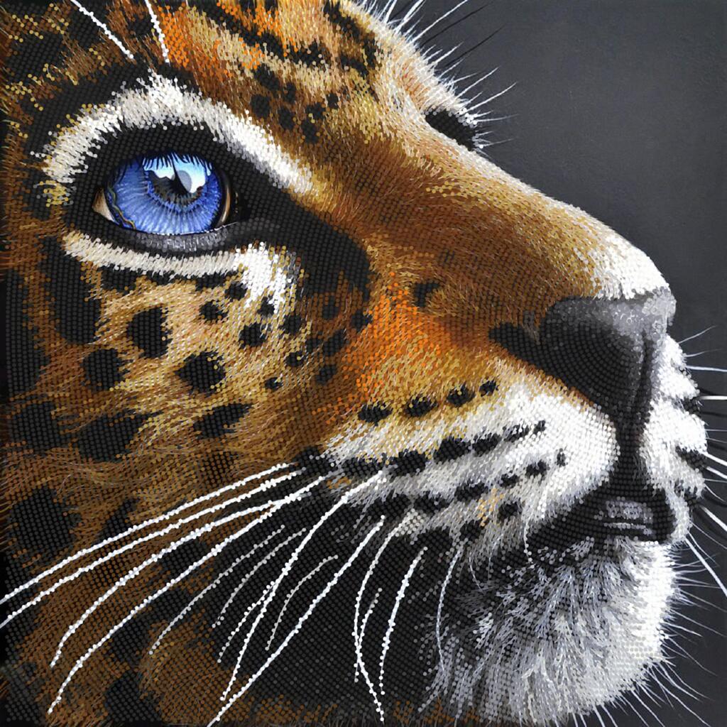 Close-up of a embroidered or painted leopard's face with detailed fur and blue eye.