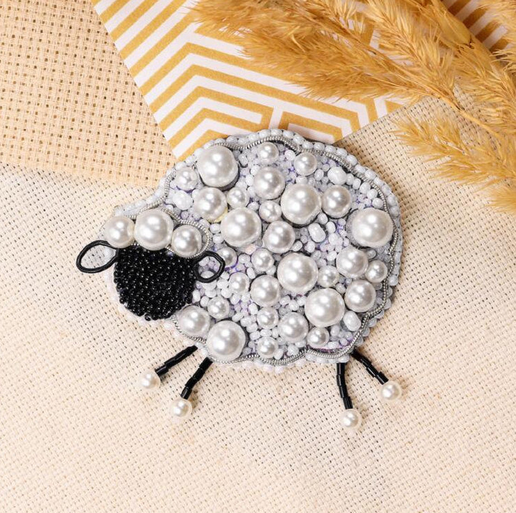 Decorative sheep-shaped object with pearls on a textured surface