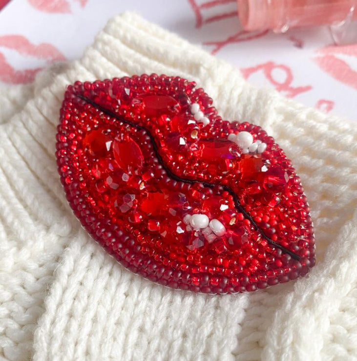 Red beaded lip-shaped brooch on a white textured fabric background