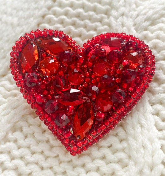 Red heart-shaped brooch with gemstones on a white textured background