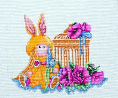 Cross stitch kit depicting a whimsical doll with rabbit ears, accompanied by flowers and a building, on unprinted Aida linen canvas.