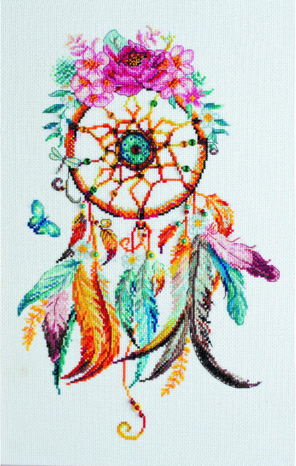 A cross stitch kit depicting a colorful dreamcatcher with feathers and flowers on a white background.