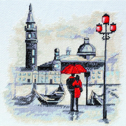 Cross stitch kit depicting a scene with a couple under a red umbrella, a boat, and a clock tower.