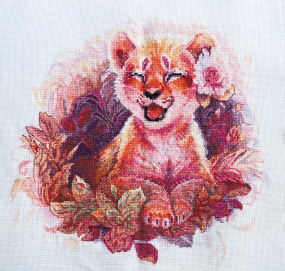 A cross stitch kit depicting a stylized little lion with floral elements, unprinted canvas.
