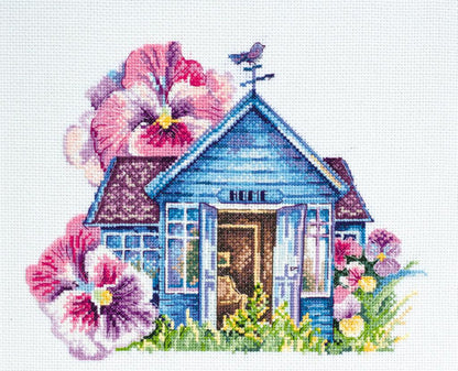 A cross stitch kit depicting a small blue house with pink flowers and a bird.