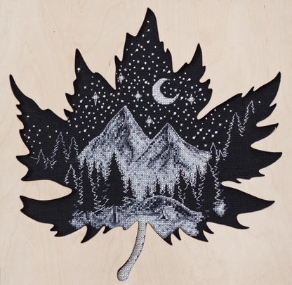 A cross stitch kit depicting a night mountain scene with a crescent moon, stars, and a forest silhouette on a unprinted canvas background.