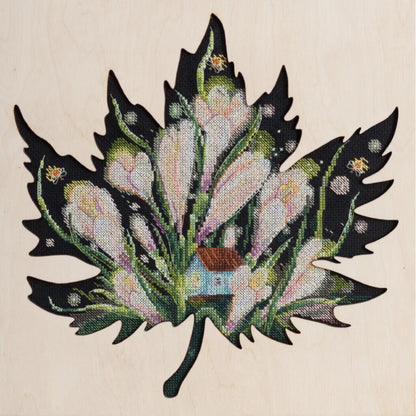 A cross stitch kit depicting a floral design on a leaf-shaped canvas.