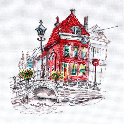 A cross stitch kit depicting a scene with a red building, a bridge, and a street lamp.
