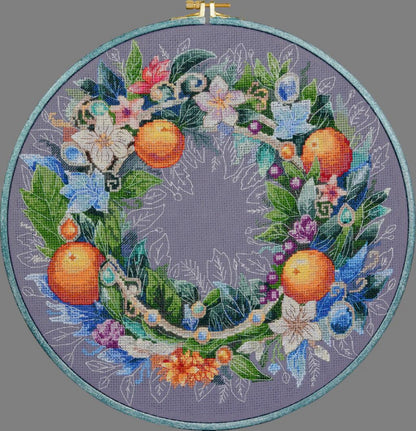 A cross stitch kit depicting a floral wreath with oranges and various flowers, surrounded by a blue border.
