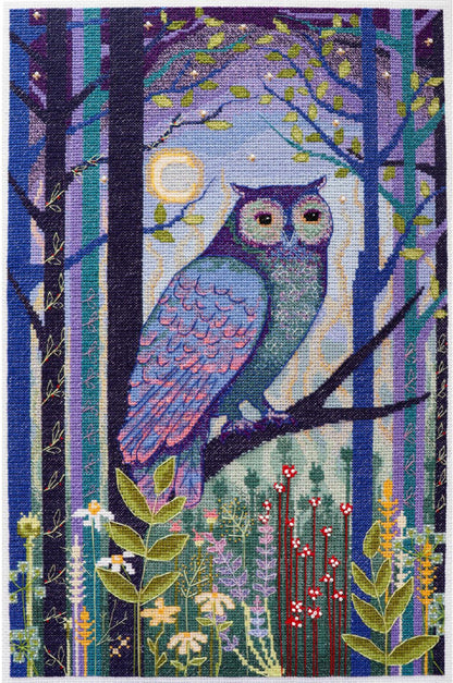 A cross stitch kit depicting an owl perched on a branch with a moon and trees in the background, surrounded by flowers.
