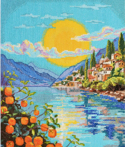 Cross-stitched landscape with a village by a lake, mountains, and oranges on a branch.