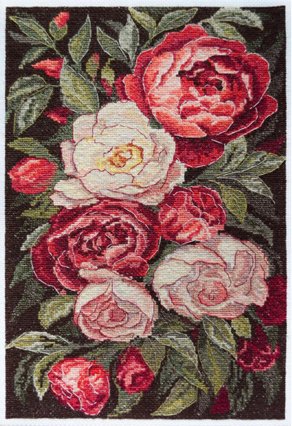 A completed cross stitch kit depicting a bouquet of roses in shades of red, pink, and white with green leaves on a dark background.