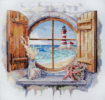 A completed counted cross stitch kit depicting a window with a view of a lighthouse, the sea, and beachcomber's treasures.