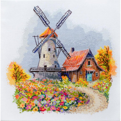 A completed counted cross stitch kit depicting a windmill and a house surrounded by autumn flowers.