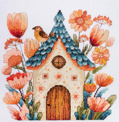 A cross stitch kit depicting a small bird perched on top of a house, surrounded by colorful flowers.