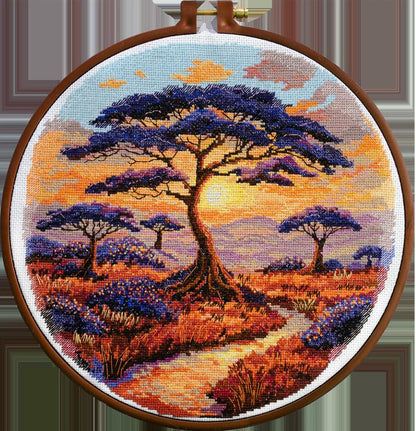 A completed cross stitch kit depicting a landscape with trees against a sunset, displayed in a hoop.