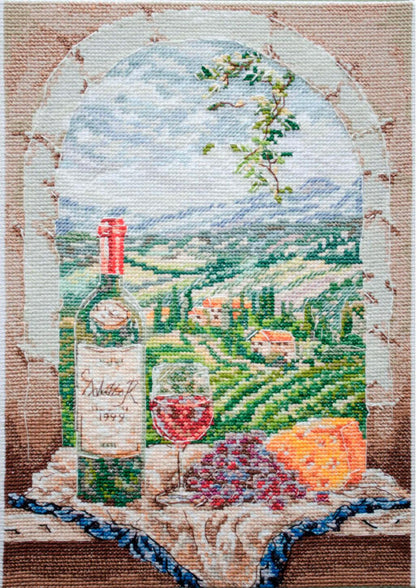 Cross stitch kit depicting a wine bottle, glass, and grapes with a scenic landscape in the background.