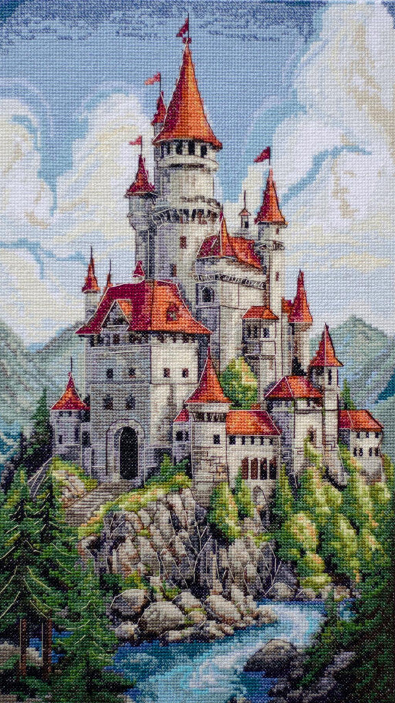 Cross-stitched castle with red roofs and flags on a mountain landscape
