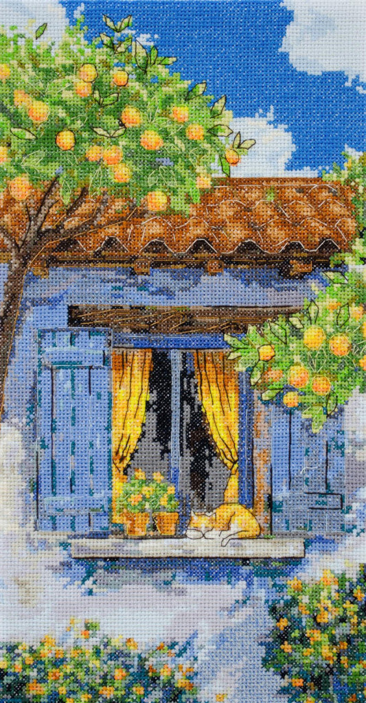 Cross-stitched scene of a cat sleeping on a windowsill with orange trees and a blue sky.