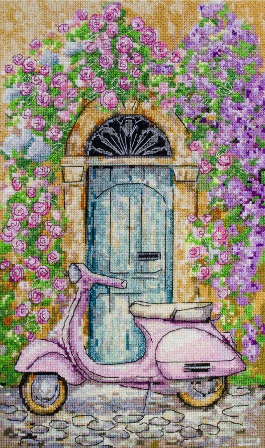 Cross-stitched design of a pink scooter in front of a floral archway