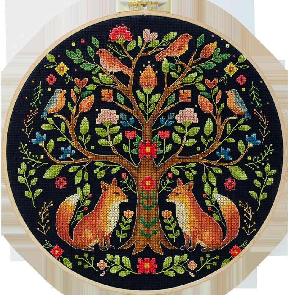 Embroidery hoop with a colorful tree design featuring birds and foxes on a black background.