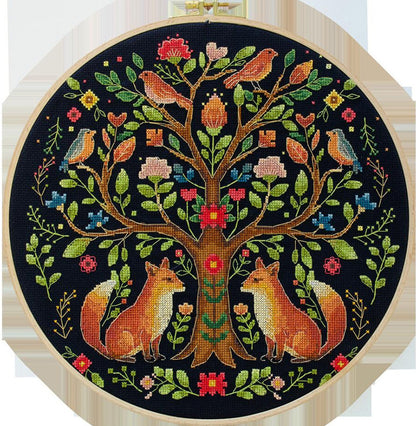 Embroidery hoop with a colorful tree design featuring birds and foxes on a black background.