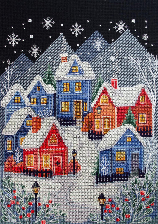 Cross-stitched village scene with snow-covered houses and trees at night.