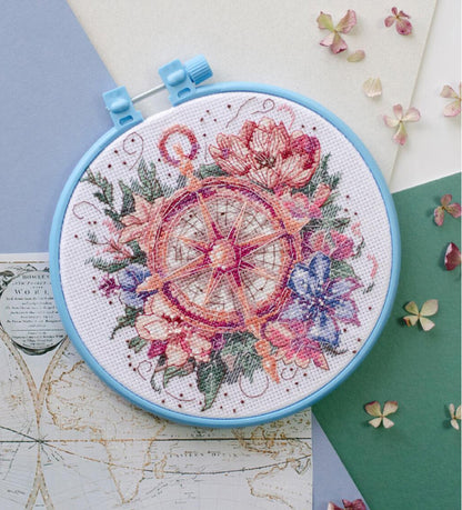A cross stitch kit depicting a flower compass, with colorful flowers and a compass rose design, displayed in an embroidery hoop.