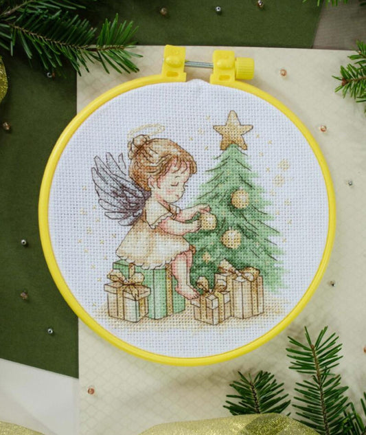Cross-stitched design of a fairy decorating a Christmas tree in an embroidery hoop.