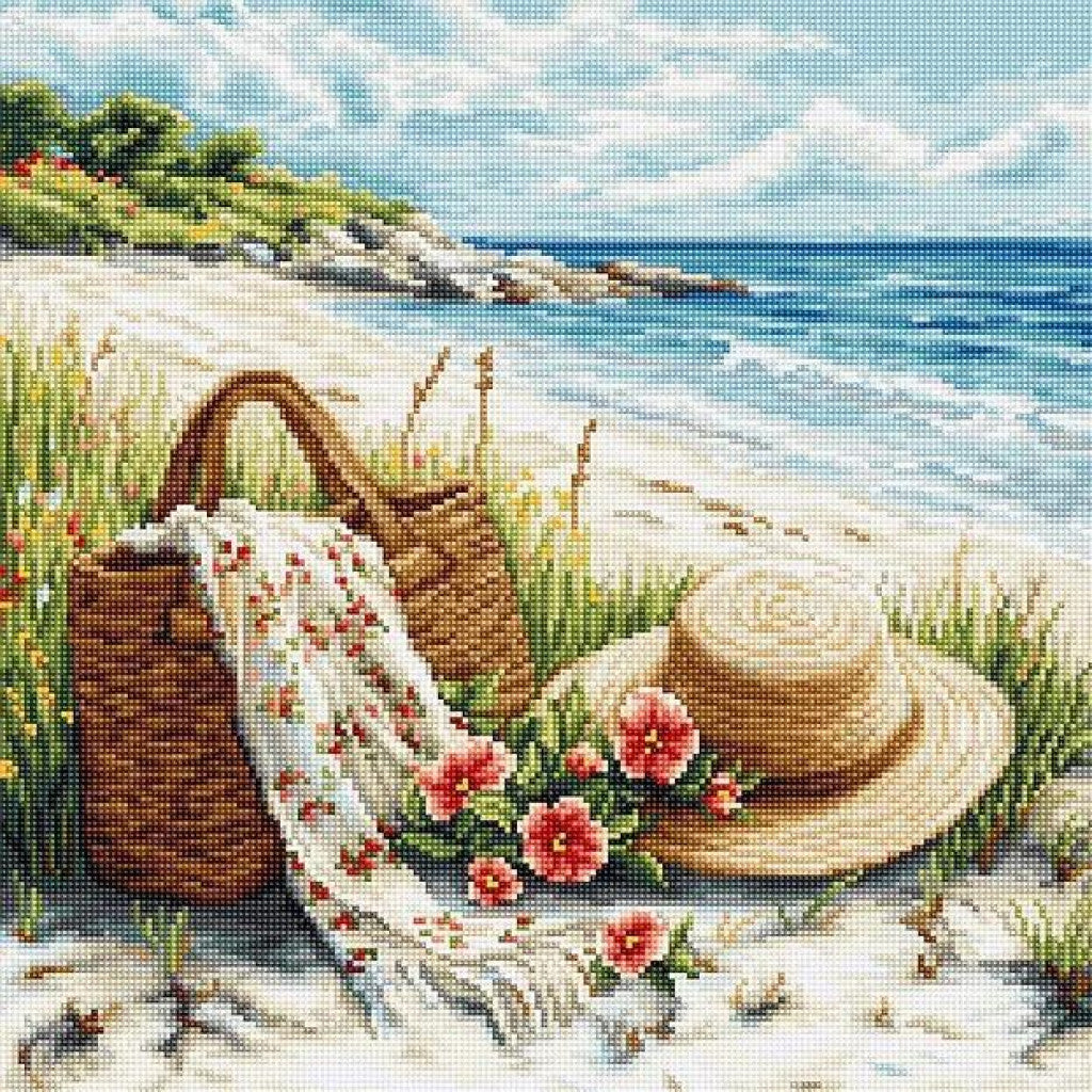 A beach-themed needlepoint or cross-stitch style scene showing a straw hat, woven basket, white blanket with pink flowers, and a sandy shoreline with blue ocean and sky.