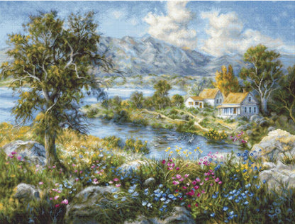 A tapestry embroidery kit depicting a scenic view of a cottage among flowers with mountain ranges in the background.