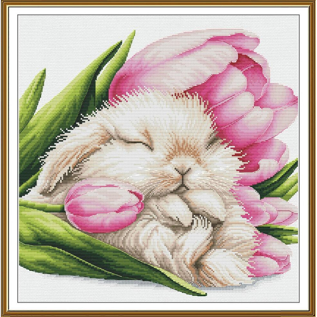 A framed needlepoint or cross-stitch style artwork showing a sleeping white bunny nestled among pink tulips and green leaves on a white canvas background, bordered by a gold frame.