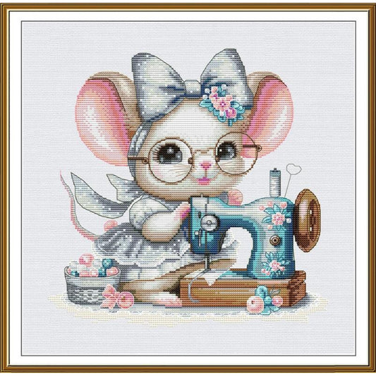 A framed cross-stitch style illustration of a cute mouse wearing round glasses and a large bow, sewing with a blue floral sewing machine. The artwork is centered on a white background with a gold-toned frame border.