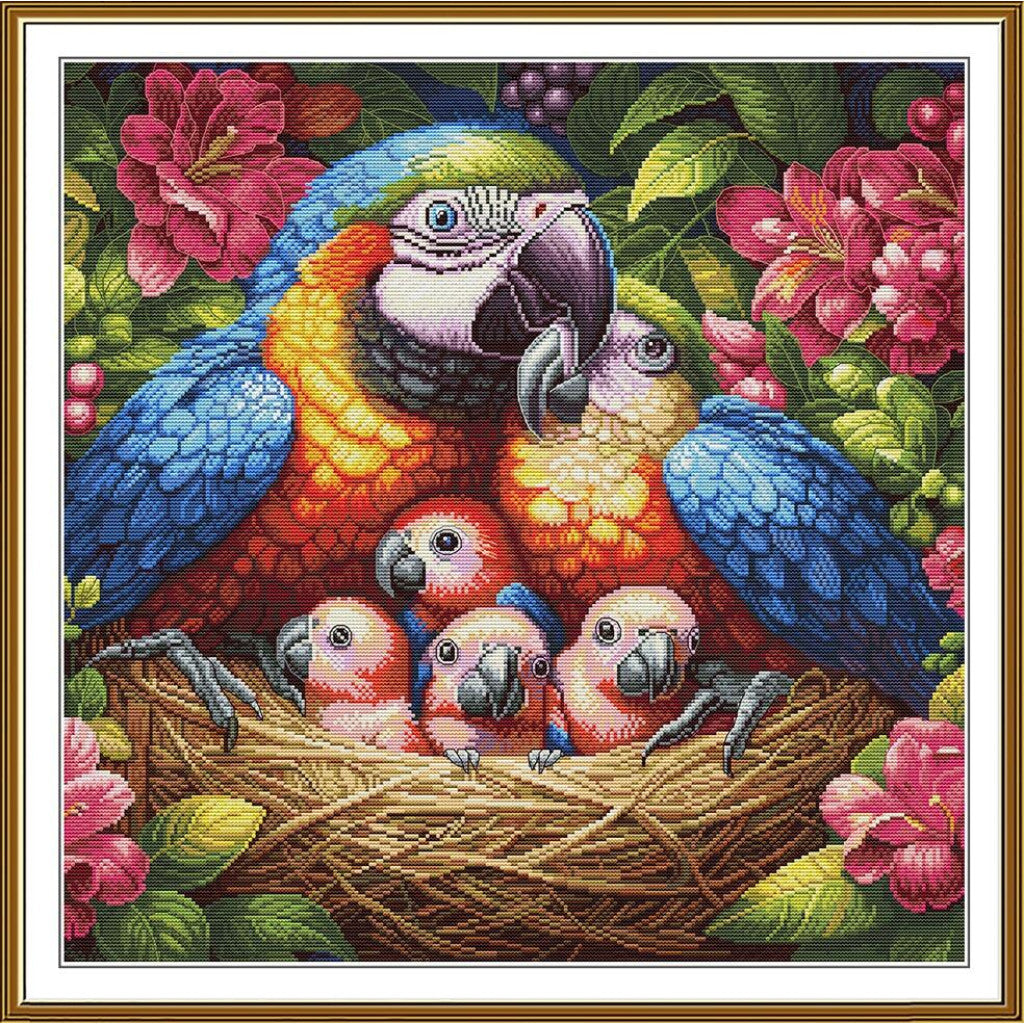 A framed cross-stitch or needlework-style artwork showing a blue-and-yellow macaw, a smaller parrot, and three chicks in a nest surrounded by pink flowers and green leaves.