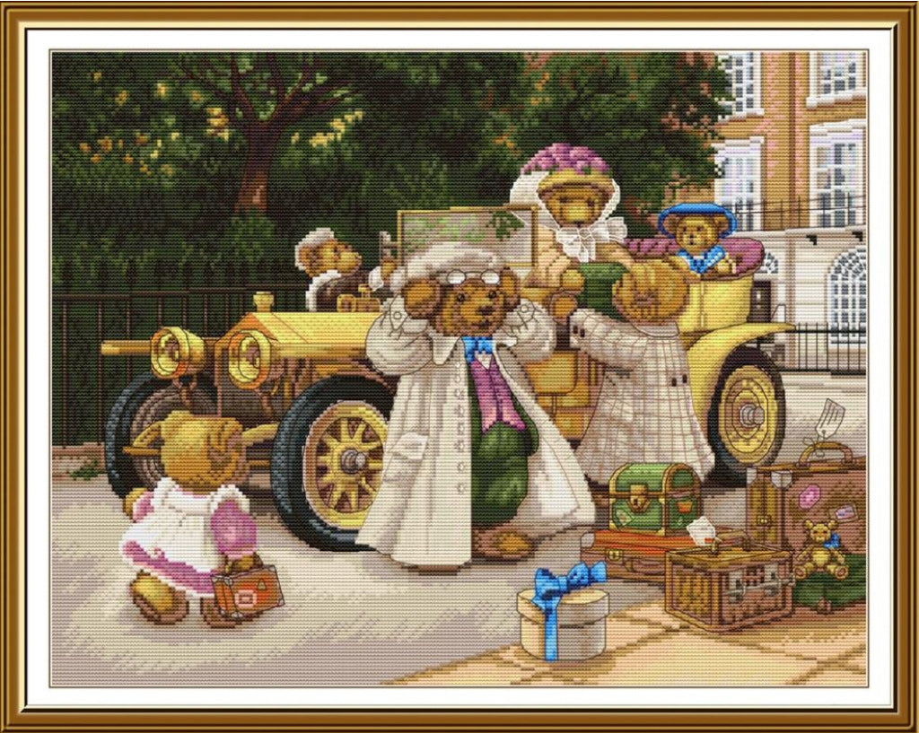 A framed cross-stitch or needlework-style illustration showing teddy bears in an outdoor street scene with vintage cars, luggage, and a gift box. The artwork is enclosed in a white mat and a warm brown wooden frame.