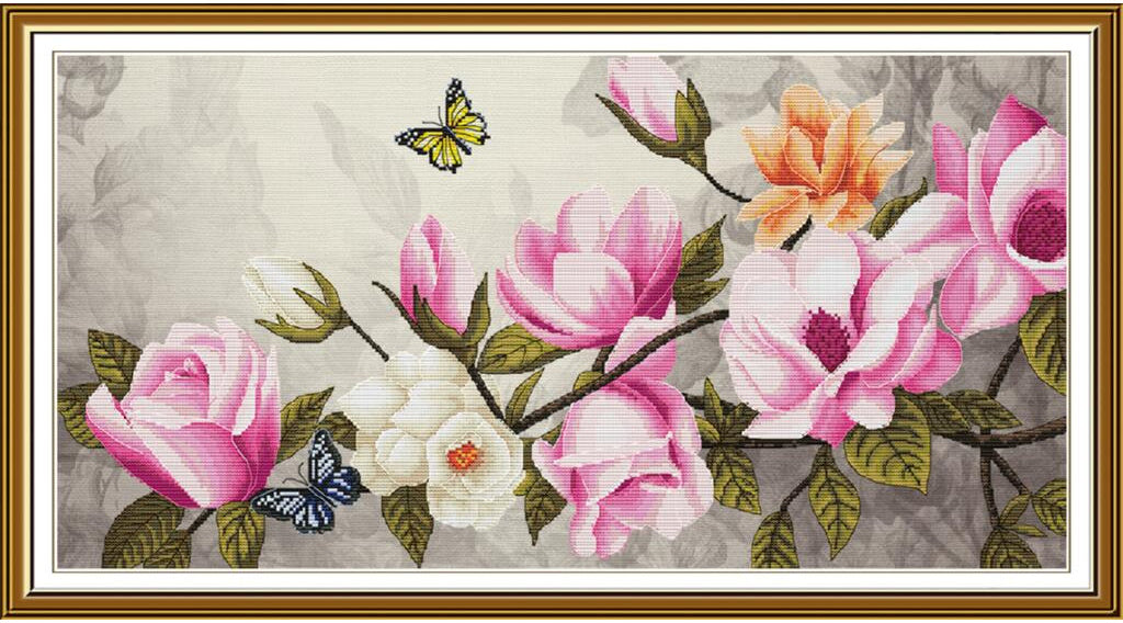 A framed floral needlepoint or cross-stitch style artwork showing pink and white magnolia blossoms, green leaves, and two small butterflies on a light gray patterned background, enclosed in a gold-toned frame.