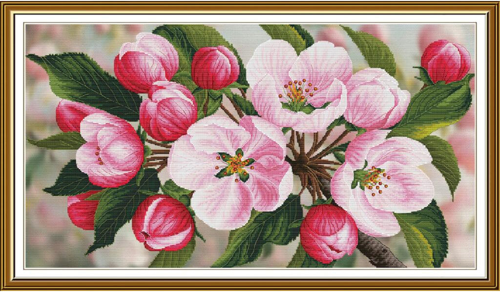 A framed floral artwork depicting pink blossoms and green leaves on a branch, shown against a soft blurred background with a gold-toned frame.