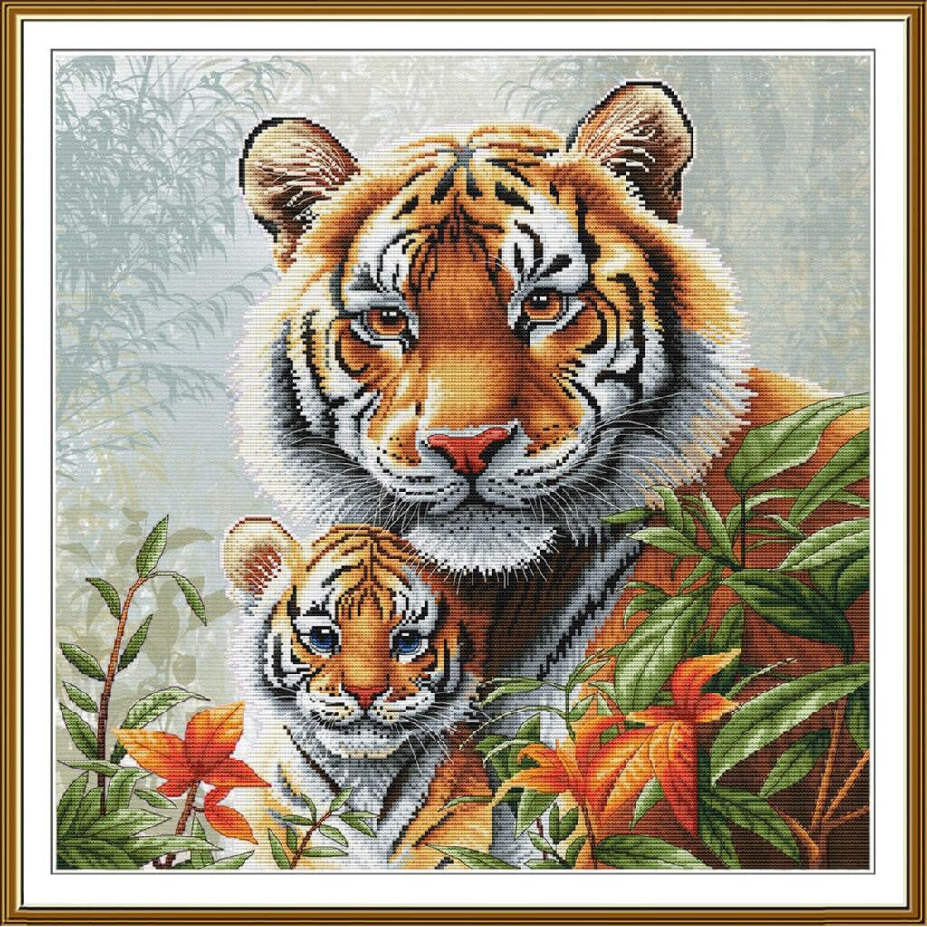 A framed cross-stitch or needlework-style tiger artwork showing an adult tiger and cub surrounded by green leaves and orange flowers, with a white mat and gold-toned frame.