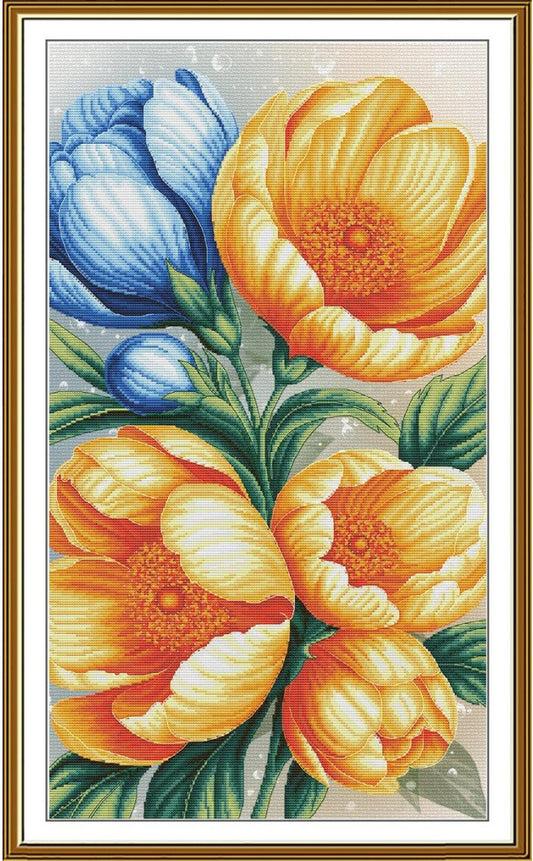 A framed floral needlepoint or cross-stitch style artwork showing large yellow-orange flowers, blue flower buds, and green leaves on a light background, surrounded by a gold-toned frame.