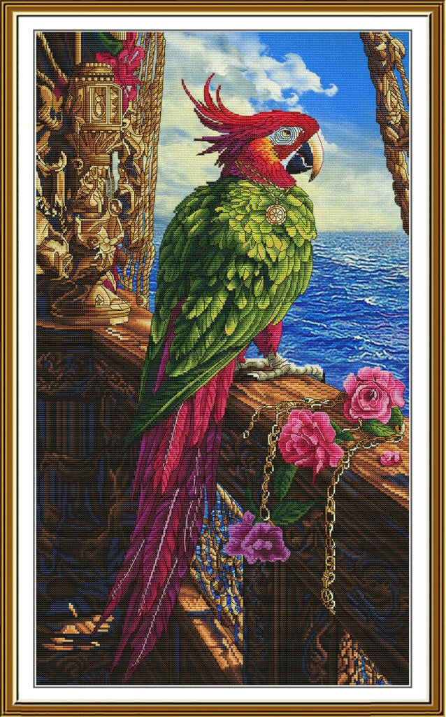 A framed needlework or cross-stitch style artwork showing a green and red parrot perched on a ship's railing with blue ocean water, clouds, pink roses, and ornate gold-toned ship details in the background.