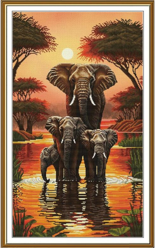 A framed vertical art print depicting a family of elephants standing in reflective water at sunset, with acacia trees and a warm orange sky.