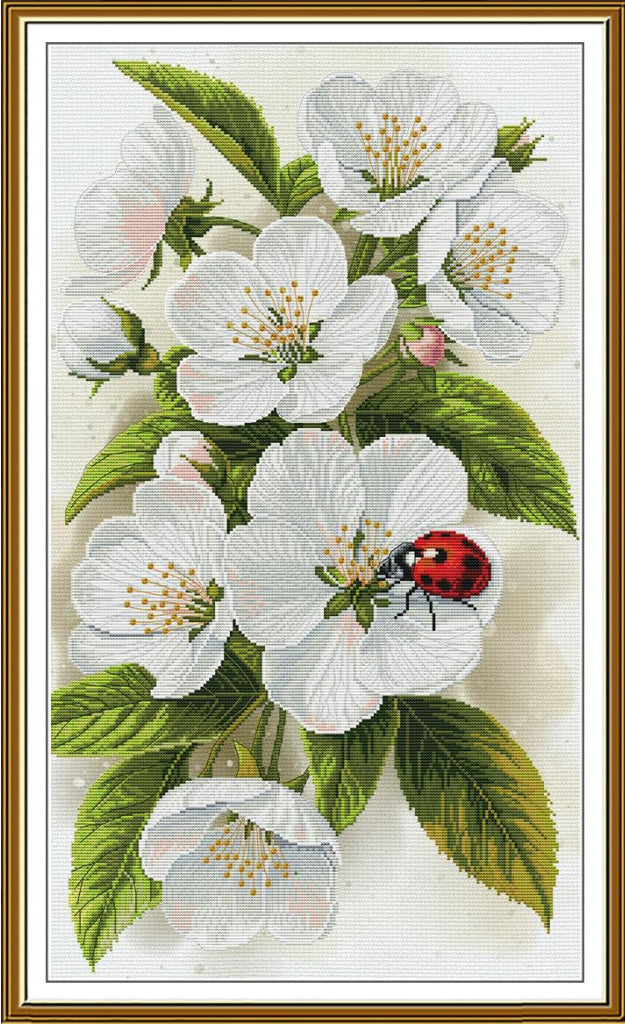 A framed botanical artwork showing white blossoms with green leaves and a small red ladybug on a cream background, enclosed in a gold-toned frame.
