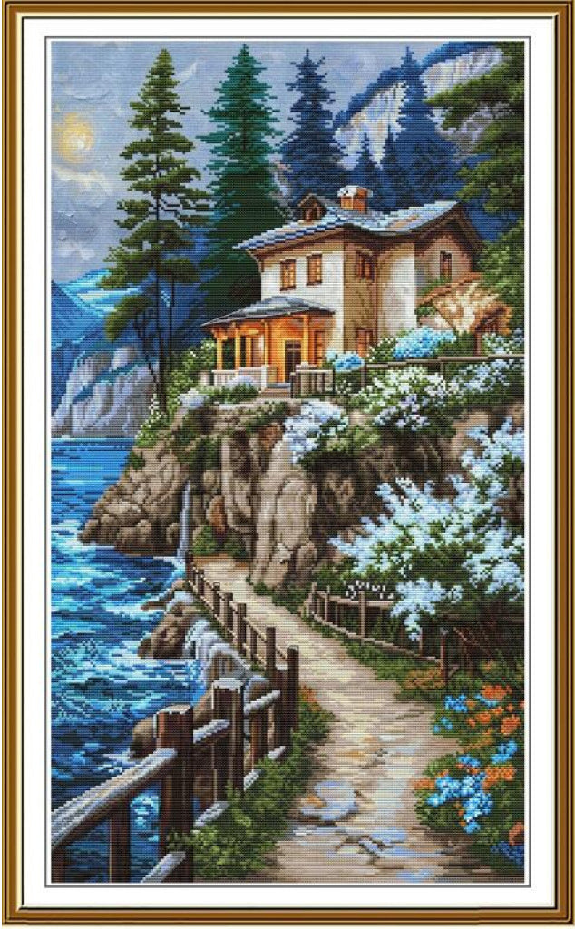 A framed vertical landscape painting depicting a coastal hillside villa, pine trees, rocky cliffs, blue water, and a winding stone path under a moonlit sky.